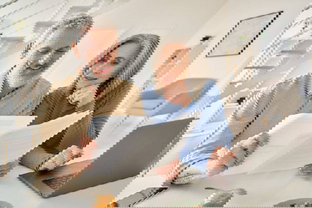 A senior couple sit at a laptop comparing multiple documents